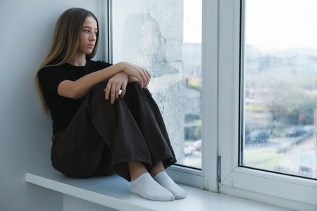 Depressed teenage girl near window at homeの写真素材