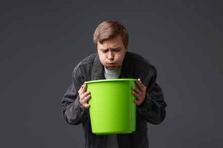 Young man with bucket suffering from nausea on gray backgroundの写真素材
