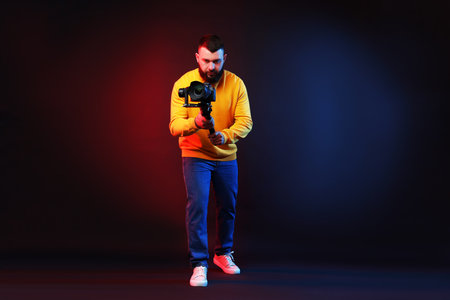 Videographer filming on camera using gimbal stabilizer against dark background with color lightsの写真素材