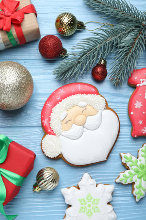 Tasty gingerbread cookies, gifts and Christmas decor on light blue wooden background, flat lay