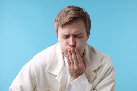 Young man suffering from nausea on light blue backgroundの写真素材