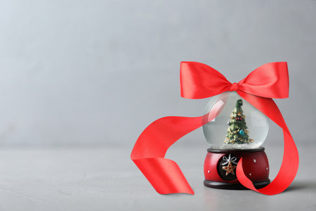 Snow globe with Christmas tree inside and red bow on gray background. Space for textの写真素材