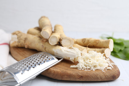 Grated horseradish, grater, leaves and fresh roots on white tiled table, closeupの写真素材