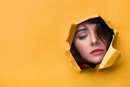 Young woman with beautiful makeup. View through torn hole in paperの写真素材