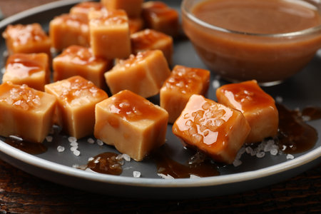 Tasty candies with salt and caramel sauce on wooden table, closeupの写真素材