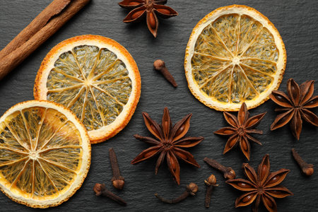 Different spices (anise, cinnamon, cloves) and dry orange slices for mulled wine on black table, flat layの写真素材
