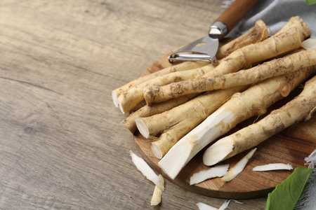 Fresh raw horseradish roots, peeler and leaves on wooden table, closeup. Space for textの写真素材