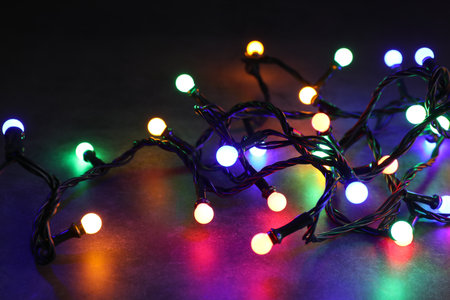 Bright Christmas lights on table in darkness, closeup. New Year greeting card