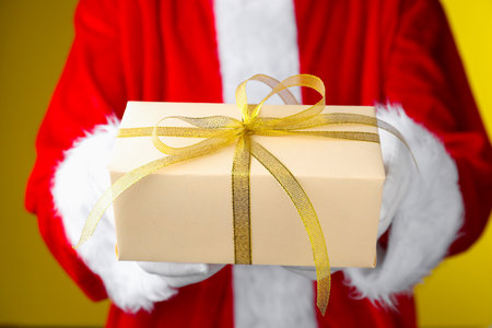 Woman in Santa costume with gift box on golden background, closeup. Merry Christmas and Happy New Yearの写真素材