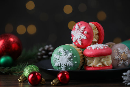 Tasty macarons and Christmas decor on black wooden table against blurred lights, closeupの写真素材