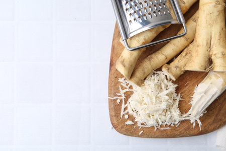 Grated horseradish, grater and fresh roots on white tiled table, top view. Space for textの写真素材