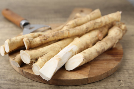 Fresh raw horseradish roots and peeler on wooden table, closeupの写真素材
