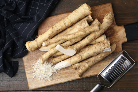 Grated horseradish, grater and fresh roots on wooden table, top view