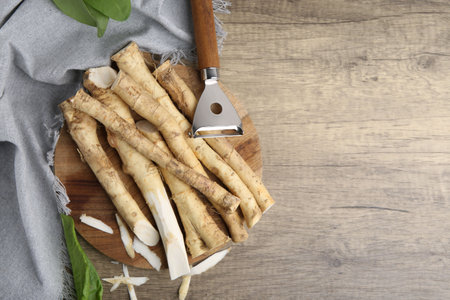 Fresh raw horseradish roots, peeler and leaves on wooden table, flat lay. Space for textの写真素材