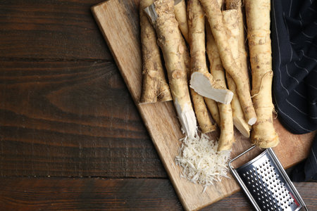 Grated horseradish, grater and fresh roots on wooden table, top view. Space for textの写真素材