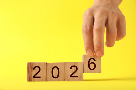 New 2026 year. Man putting cube with number 6 on yellow background, closeup