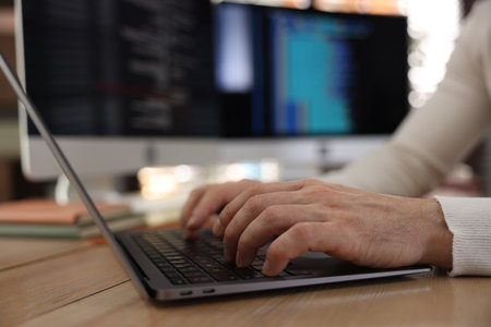 Programmer working on laptop at wooden table indoors, closeupの写真素材