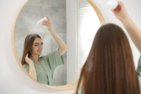 Woman using talcum powder as dry shampoo near mirror at homeの写真素材
