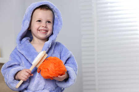 Smiling little boy in blue bathrobe with hairbrush and shower puff in the bathroom. Space for textの写真素材