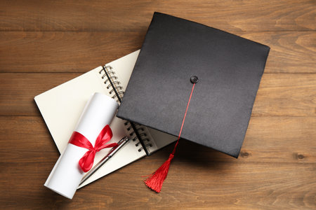 Graduation cap, diploma, notebook and pen on wooden table, top viewの写真素材