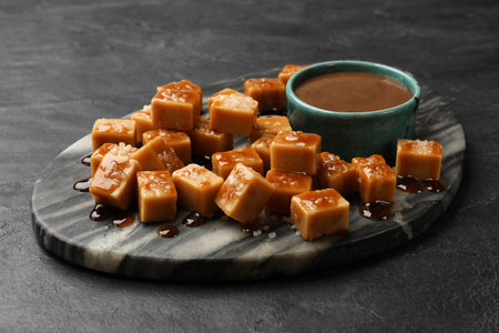 Tasty candies with salt and caramel sauce on dark textured table, closeupの写真素材