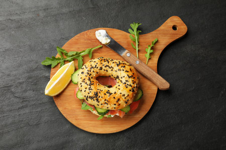 Bagel with salmon, cream cheese, cucumber, arugula and lemon on black table, top viewの写真素材