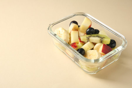 Tasty fruit salad in glass container on beige background, closeup. Space for textの写真素材