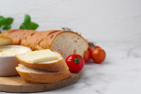 Cut baguette with butter and tomatoes on white marble table, closeup. Space for textの写真素材