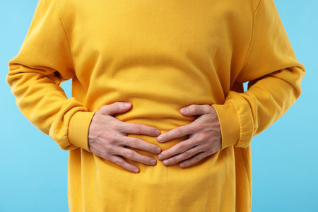 Young man suffering from nausea and stomachache on light blue background, closeup
