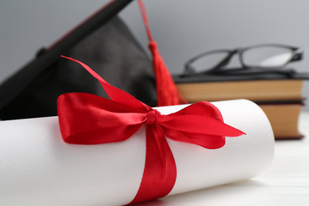 Graduation cap, diploma, glasses and books on white wooden table against light background, selective...