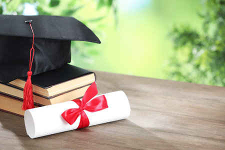 Graduation cap, diploma and books on wooden table against blurred background, closeup. Space for textの写真素材