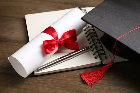 Graduation cap, diploma, notebook and pen on wooden table, closeupの写真素材