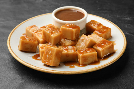 Tasty candies with salt and caramel sauce on dark textured table, closeupの写真素材