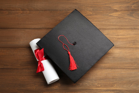Graduation cap and diploma on wooden table, top viewの写真素材