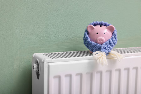 Piggy bank with scarf on heating radiator near green wall, closeupの写真素材