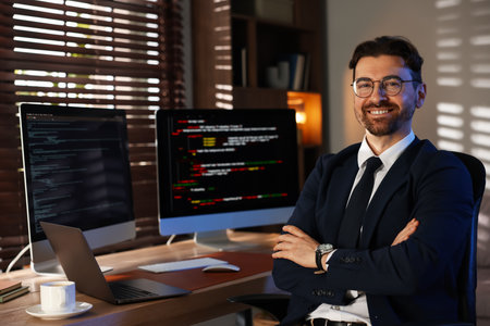 Portrait of smiling programmer in glasses and suit with crossed arms on chair at workplaceの写真素材