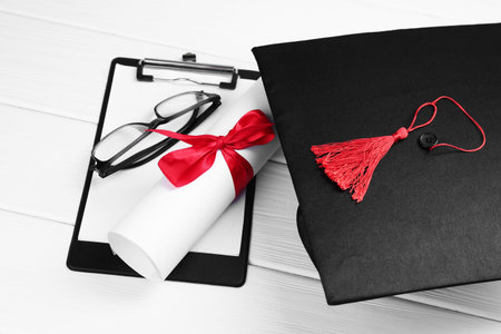Graduation cap, diploma, glasses and clipboard on white wooden table, closeupの写真素材
