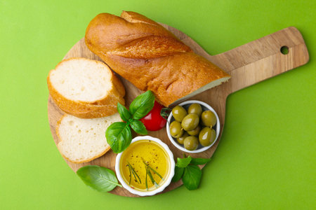 Tasty baguette served with oil, tomato, olives and basil on green background, top viewの写真素材