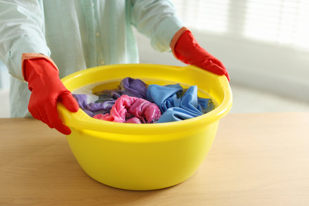 Woman washing clothes in plastic basin at wooden table indoors, closeup. Space for textの写真素材