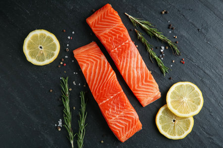 Pieces of salmon fillet, spices and lemon on black textured table, flat layの写真素材