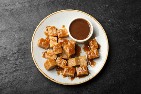 Tasty candies with salt and caramel sauce on dark textured table, top view