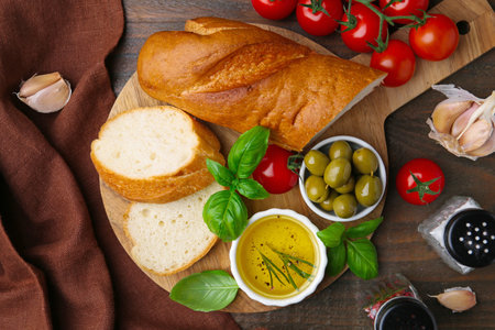 Tasty baguette served with oil, tomatoes, olives and basil on wooden table, flat layの写真素材