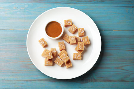 Tasty candies with salt and caramel sauce on light blue wooden table, top viewの写真素材