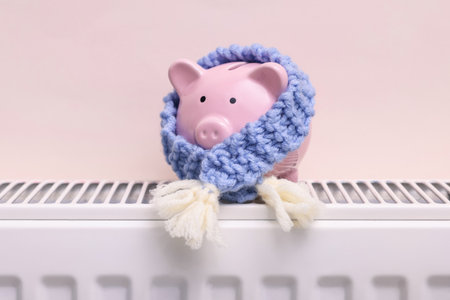 Piggy bank with scarf on heating radiator near beige wall, closeupの写真素材