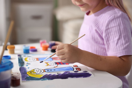 Little girl with brush drawing at white table indoors, closeupの写真素材
