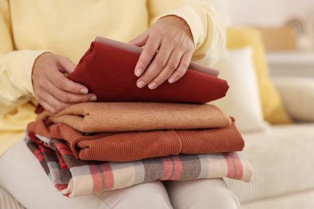 Woman with stack of clothes on sofa indoors, closeup
