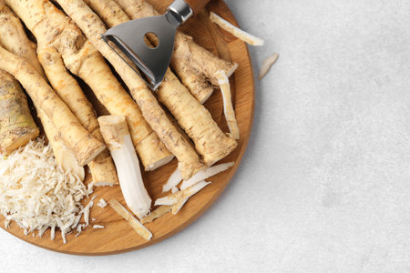 Whole and gratified horseradish roots near peeler on light gray table, top view. Space for textの写真素材
