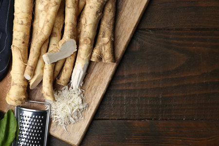 Grated horseradish, grater, leaves and fresh roots on wooden table, flat lay. Space for textの写真素材