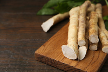Fresh raw horseradish roots and leaves on wooden table, closeup. Space for textの写真素材