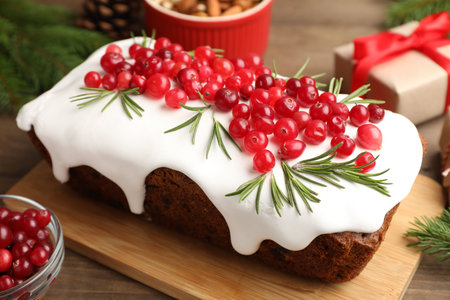 Tasty Christmas cake with icing, cranberries, rosemary and festive decor on wooden table, closeupの写真素材